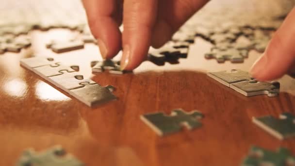 Caucasian woman hands assembling jigsaw puzzle pieces. Single pieces and complete puzzle at background. Warm colors - Footage, Video