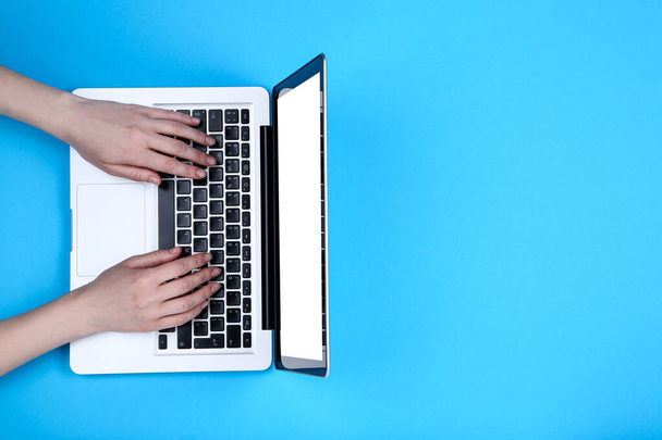 Female hands typing on laptop keyboard on blue background - Foto, Imagen