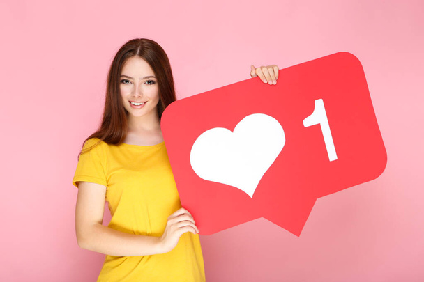 Young woman holding paper card with heart and number one on pink background - Foto, Imagen