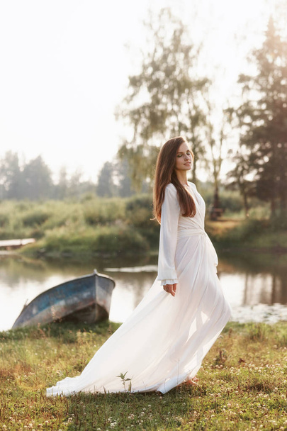 Beautiful slender woman in a long white dress walks in the morni - Fotoğraf, Görsel