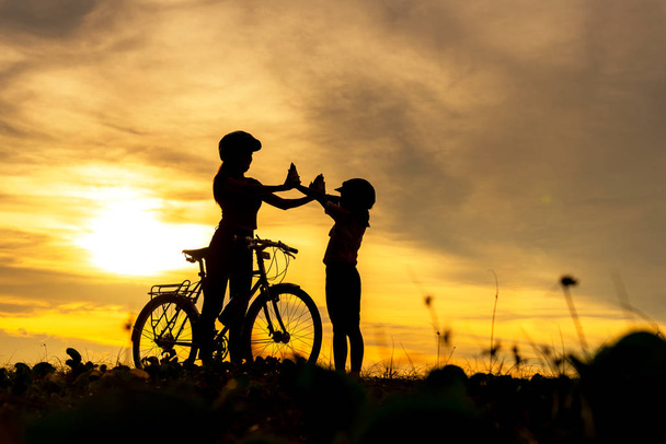 Sylwetka rowerzysta piękne rodziny podnieść dać mi pięć o zachodzie słońca dla relaksu i wolności. Mama i córka na rowerze na plaży. Koncepcja stylu życia. - Zdjęcie, obraz