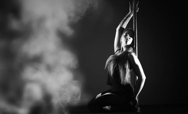 Girl doing exercises on a sports equipment. The dancer on the pylon in the studio. - Foto, Bild