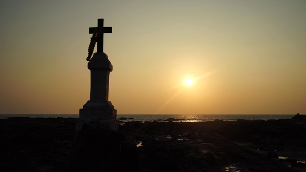 Ο χριστιανικός σταυρός στους βράχους δίπλα στη θάλασσα με θέα το ηλιοβασίλεμα - Πλάνα, βίντεο