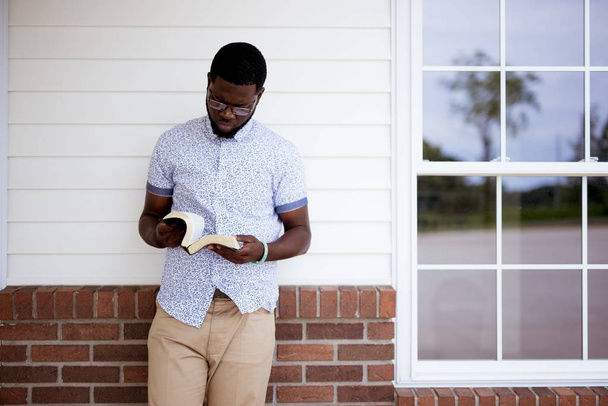 Male leaning against a wall while reading the bible - Foto, Imagen