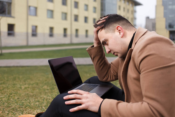 Un uomo seduto con un portatile e depresso a causa del lavoro. Studente pensieroso tiene la testa
 - Foto, immagini