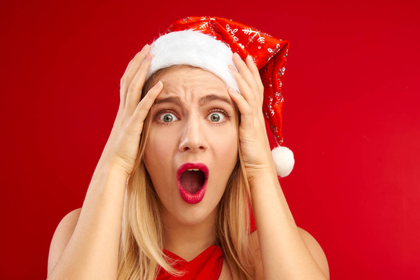 Shocked surprised girl in santa claus hat isolated on festive red background with copy space, time to buy gifts for christmas and new year, discounts and sale - Foto, Bild