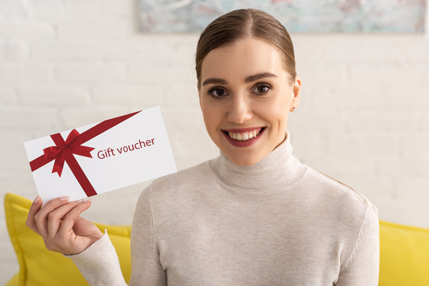 Beautiful smiling woman looking at camera and showing gift voucher - Foto, imagen
