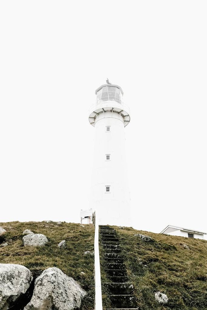 Vertical shot of a white lighthouse on top of a grassy hill - Foto, afbeelding