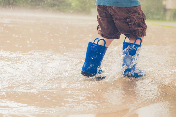 Closeup shot of the legs of a boy in blue rubber boots splashing in a puddle - Fotografie, Obrázek