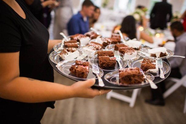 Servírka servíruje čokoládové dorty na černém podnosu v restauraci - Fotografie, Obrázek