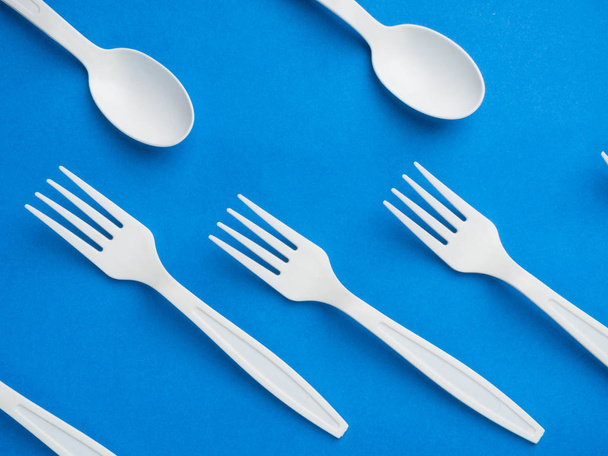 Plastic white disposable fork and spoon on a trendy blue color background. Concept plastic dishes, fast food, plastic pollution. Top view, flat lay. - Photo, Image