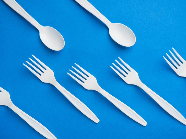 Plastic white disposable fork and spoon on a trendy blue color background. Concept plastic dishes, fast food, plastic pollution. Top view, flat lay. - Photo, Image