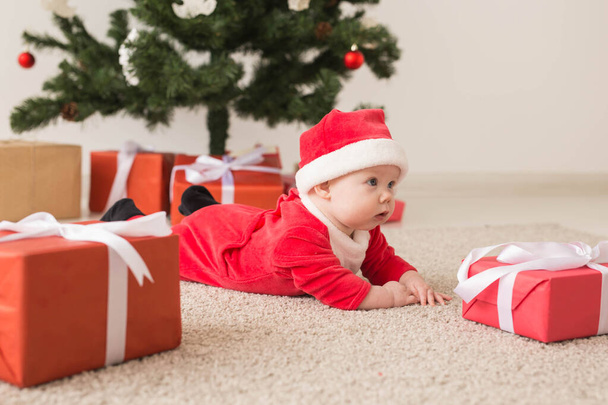 Cute baby girl wearing santa claus suit crawling on floor over Christmas tree. Holiday season. - Photo, image