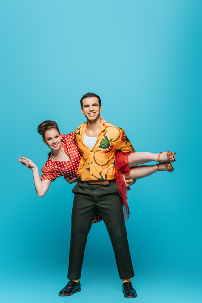handsome dancer holding partner while dancing boogie-woogie on blue background - Photo, Image