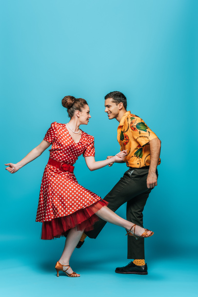 smiling dancers looking at each other while dancing boogie-woogie on blue background - Photo, Image