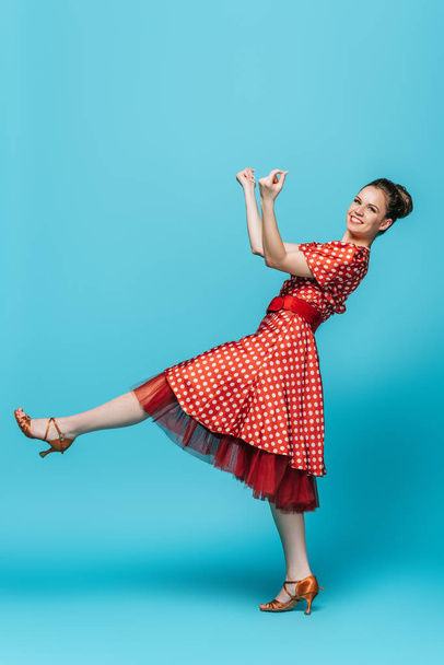 pretty, stylish dancer looking at camera while dancing boogie-woogie on blue background - Фото, изображение
