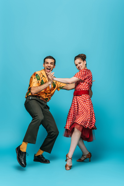 cheerful dancers holding hands while dancing boogie-woogie on blue background - Fotó, kép