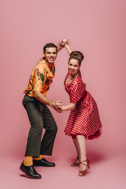 smiling dancers looking at camera while dancing boogie-woogie on pink background - Photo, Image