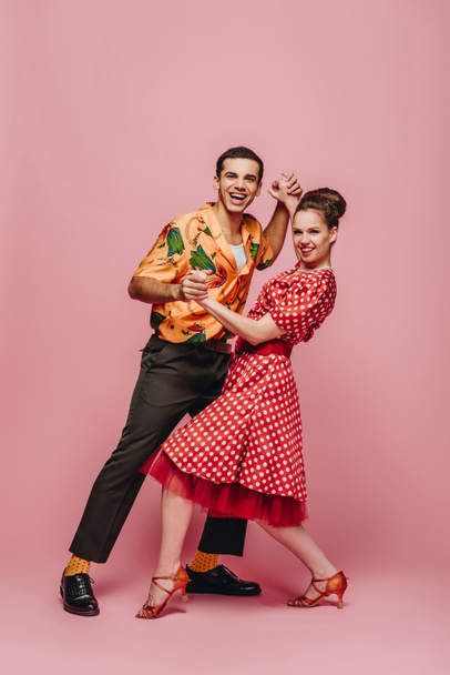elegant dancers holding hands while dancing boogie-woogie on pink background - Foto, immagini