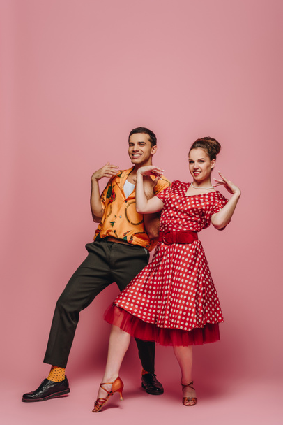 elegant dancers looking at camera while dancing boogie-woogie on pink background - Photo, Image