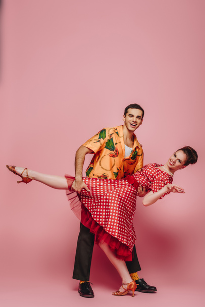 elegant dancer supporting partner while dancing boogie-woogie on pink background - Photo, Image