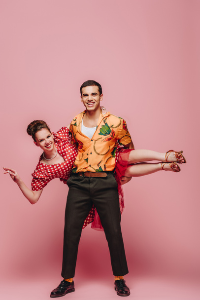 handsome dancer holding woman while dancing boogie-woogie on pink background - Photo, image