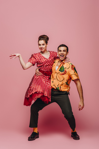 stylish dancer holding woman while dancing boogie-woogie on pink background - Photo, Image