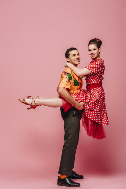 alegre hombre sosteniendo mujer mientras bailando boogie-woogie sobre rosa fondo
 - Foto, Imagen