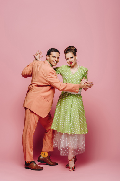 stylish dancers holding hands while dancing boogie-woogie on pink background - Fotó, kép