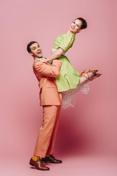 stylish dancer holding girl while dancing boogie-woogie on pink background - Photo, Image