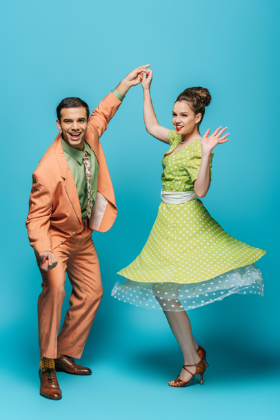 stijlvolle dansers hand in hand terwijl dansen boogie-woogie op blauwe achtergrond - Foto, afbeelding