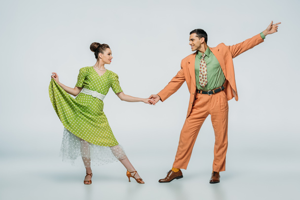 stylish dancers holding hands and looking at each other while dancing boogie-woogie on grey background - Photo, Image