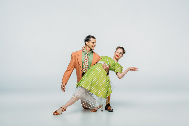 handsome dancer standing on knee and supporting partner while dancing boogie-woogie on grey background - Foto, imagen