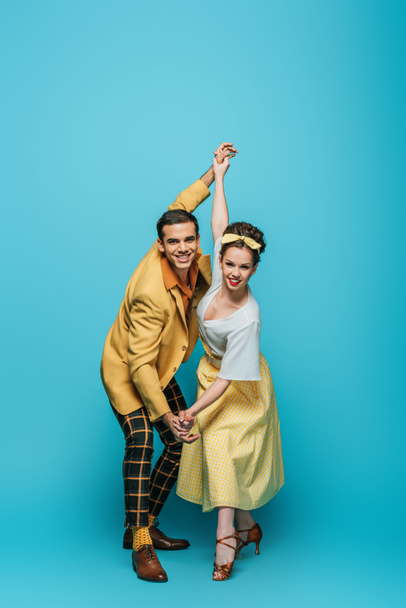 stylish dancers holding hands while dancing boogie-woogie on blue background - Photo, Image