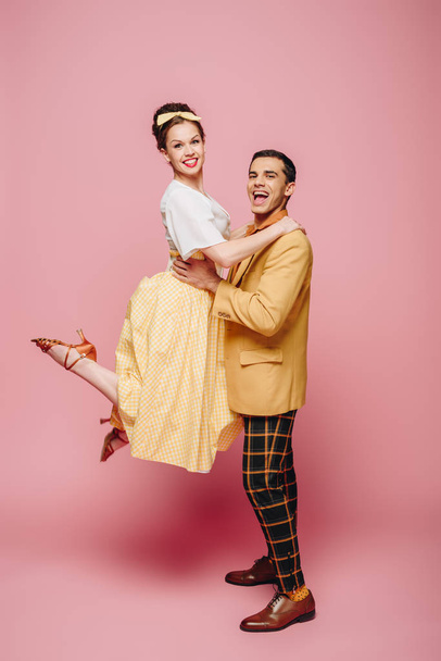 knappe man holding meisje terwijl dansen boogie-woogie op roze achtergrond - Foto, afbeelding