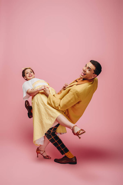 cheerful couple looking at camera while dancing boogie-woogie on pink background - Photo, Image