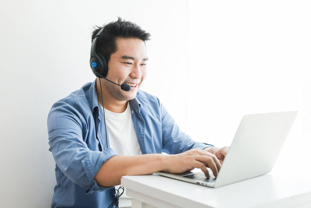Asiatique bel homme en chemise bleue à l'aide d'un ordinateur portable avec casque tal
 - Photo, image