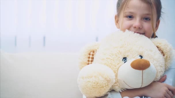 Happy little girl sitting on the sofa, hugging a big teddy-bear. - Кадри, відео