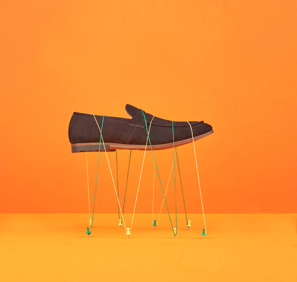 soaring male leather shoe held by threads on a orange yellow background. - Фото, зображення