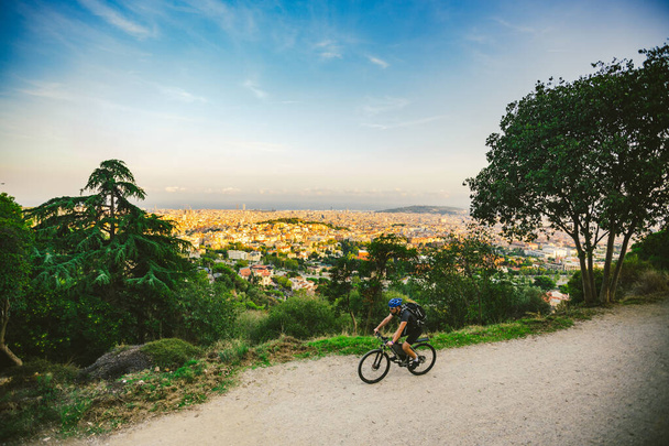 The theme of outdoor activities, sports lifestyle in nature. A man riding a mountain bike cross country on a mountain mountain tibidabo with a view of Barcelona at sunset - Photo, Image