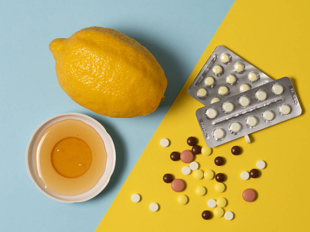 Renkli arka planlarda sağlık konsepti. Bir tarafta çeşitli ilaçlar, vitaminler ve haplar diğer tarafta ballı limon. - Fotoğraf, Görsel