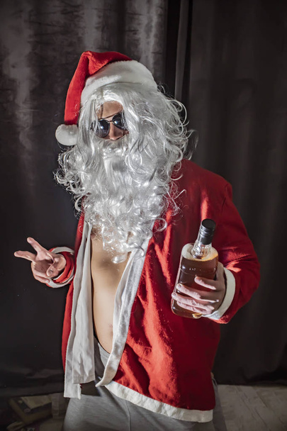 slechte santa man portret in donkere kamer, Santa Claus met een fles whisky genieten van een drankje - Foto, afbeelding