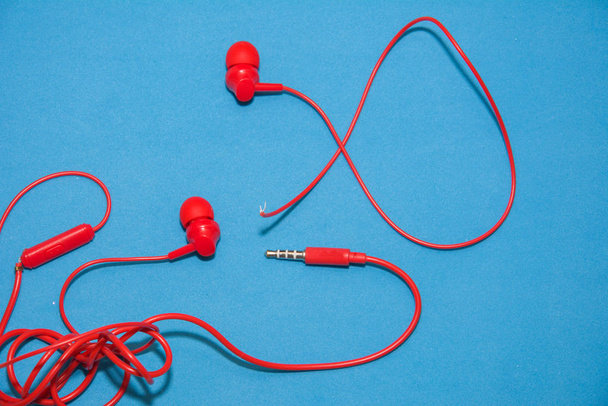 Red broken torn headphones on classic blue background. Close up broken old earphone. - Фото, зображення