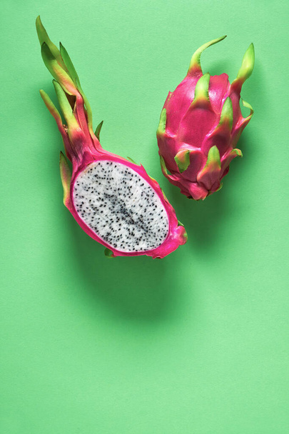 Fresh organic dragonfruit (pitaya or pitahaya) cut in half on green mint background. Creative flat layout with copy-space. Trendy exotic fruit in vibrant bold pink and green, whole and cut in half. - Фото, изображение