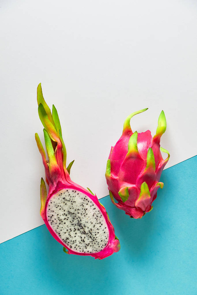 Creative flat layout with fresh organic pink, white and green dragonfruit (pitaya or pitahaya) on two tone split blue mint and white background. Trendy top view, flat lay of the fruit cut in half. - Фото, изображение