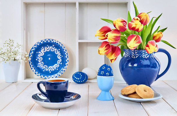 Cup of coffee and cookies on light wooden table with red tulips and springtime decorations - 写真・画像