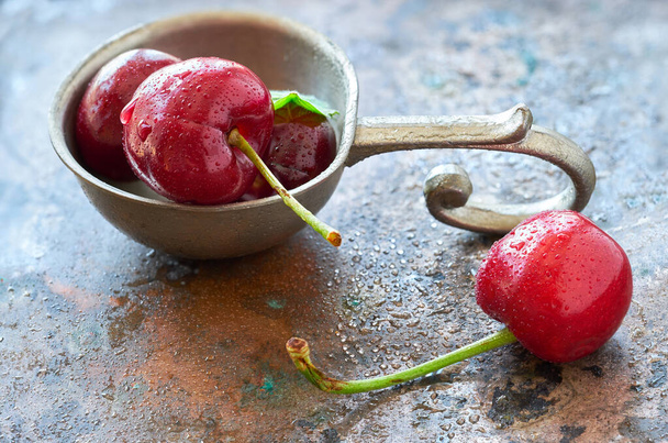 Close-up on dark cherries and fresh mint leaves in pewt bowl on grunge metal background - Foto, afbeelding