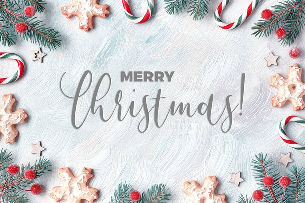 Toned Xmas frame in white, red and green. Fir twigs, candy canes, frosted berries and cookies. Light textured background, flat lay with text "Merry Christmas". - Foto, Bild