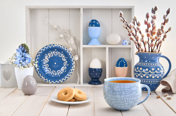 Cup of coffee and cookies on white table with bunch of pussy-willow in blue ceramic jar and matching springtime decorations - 写真・画像