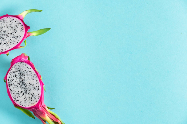 Fresh dragonfruit, pitaya or pitahaya, cut in half on blue mint background. Creative flat layout with copy-space, place for text. Trendy exotic fruit in vibrant bold pink and green colors. - 写真・画像